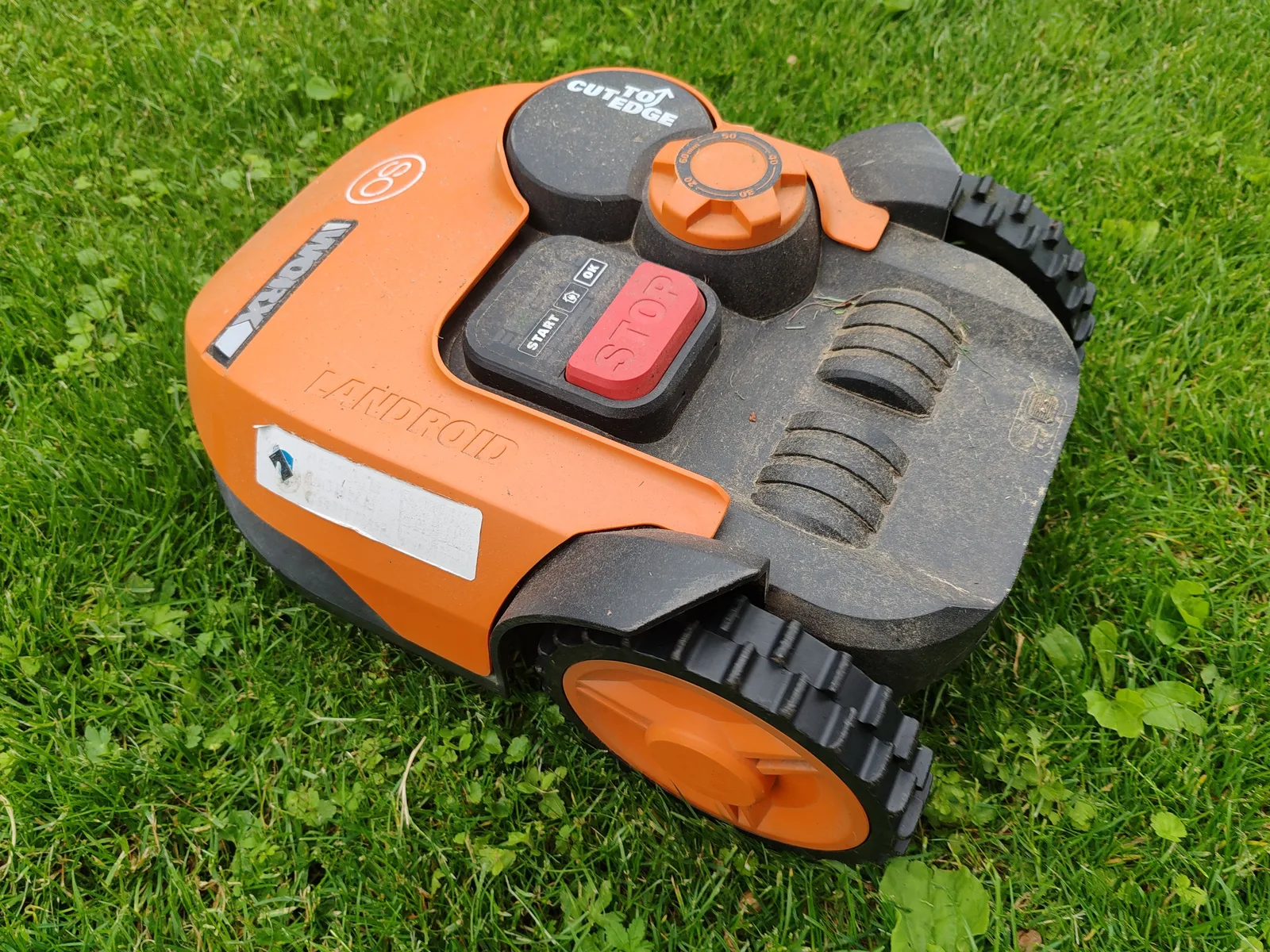 A modern robotic lawn mower in vibrant orange resting on a green lawn, ready for automated mowing tasks. Robotic Lawn Mower for Steep Slopes: What to Look For